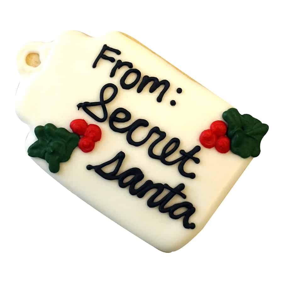 Decorated gift tag cookie with "From: Secret Santa" written in icing, with holly berry decorations.