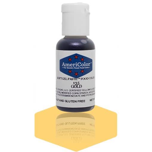 A bottle of AmeriColor Gold soft gel paste food coloring with a white cap and blue label adorned with red stars, standing on a shiny gold reflective surface that mirrors the bottle.
