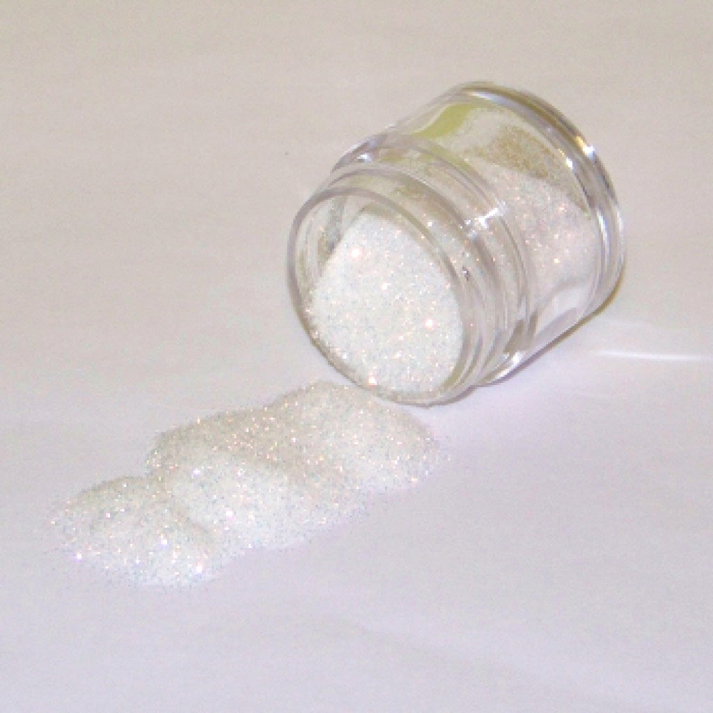 Small clear jar tipped on its side spilling gold iridescent glitter dust onto a white surface, showing fine pale gold sparkling particles with subtle rainbow highlights.