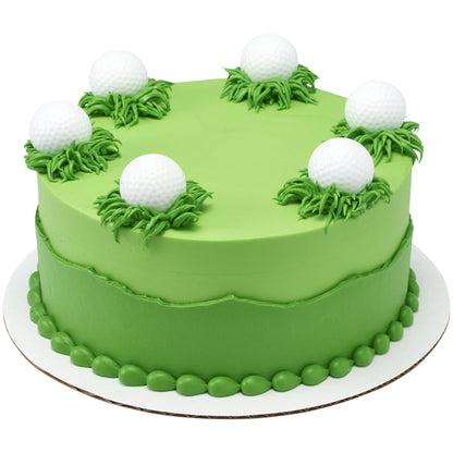 Green frosted round cake decorated with piped grass tufts and white dimpled golf ball cupcake rings placed around the top edge.