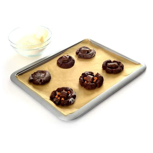 Six chocolate cookies on a baking tray with a bowl of ingredients.