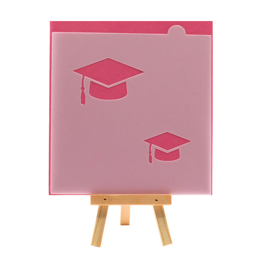 Graduation cap cookie stencil with two mortarboard designs, shown on a pink background.