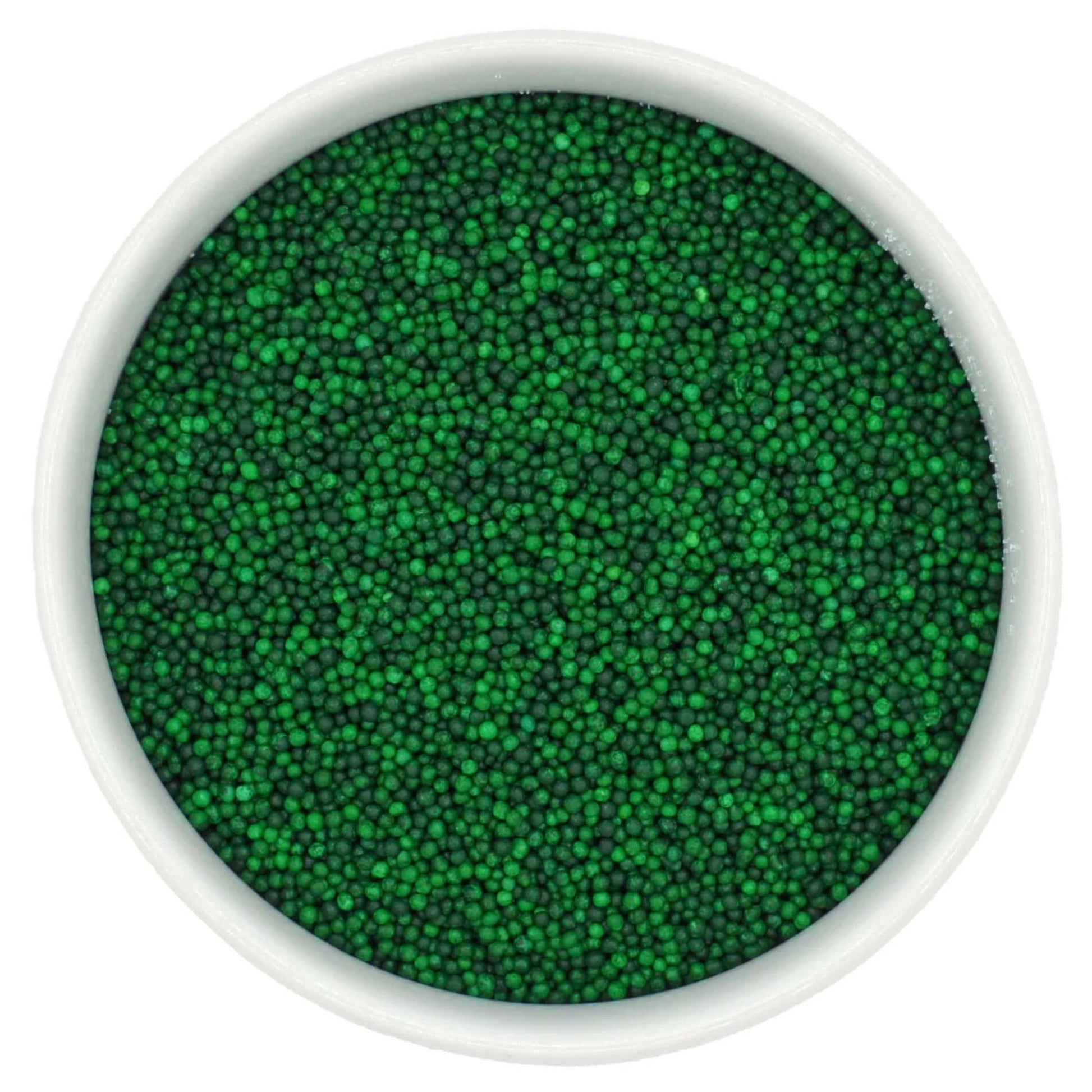 Top-down view of a white bowl filled with green non-pareils, showing tiny round sprinkle beads in mixed shades of bright and deep green.