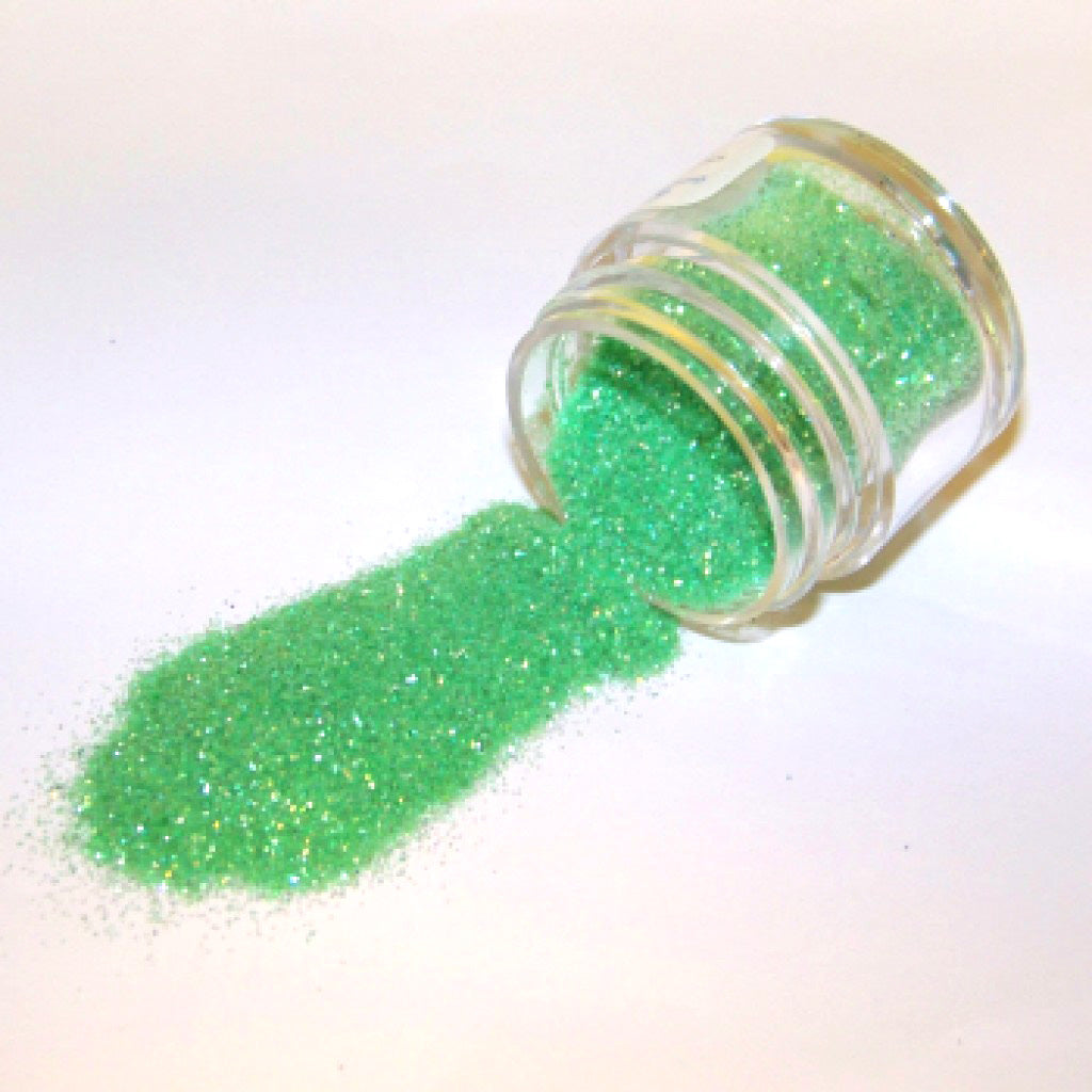 Green Rainbow Galaxy Glitter Dust spilling from a small clear jar onto a white surface, showing light green glitter with rainbow shimmer.