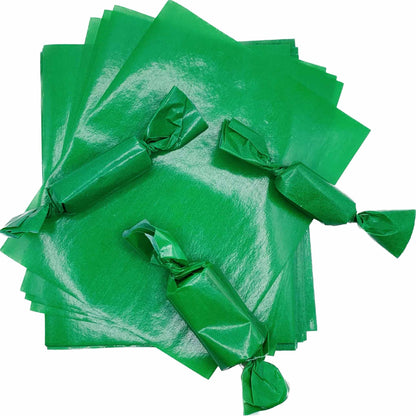 Stack of bright green 4" x 5" wax caramel wrappers with three rectangular candy pieces individually wrapped and twisted at both ends.