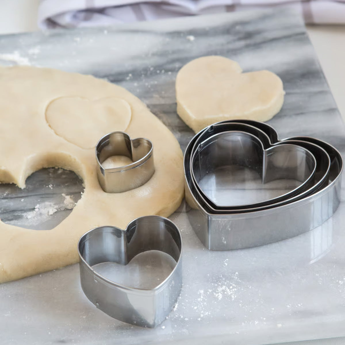 Heart cookie cutters in various sizes on a marble surface with rolled-out cookie dough.