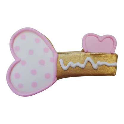 Decorated heart-shaped key cookie with pink polka dots, a gold handle, and white icing details, resembling a whimsical love key.