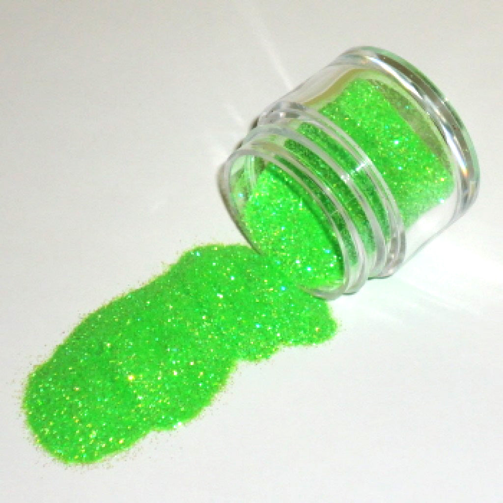 Small clear jar tipped on its side spilling bright neon green glitter dust onto a white surface.