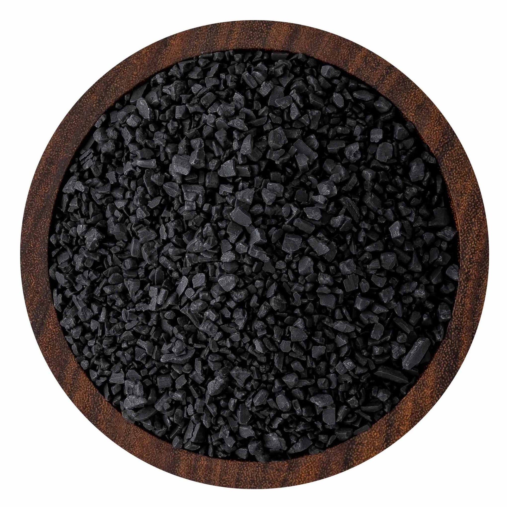 Top-down view of coarse black sea salt crystals in a round wooden bowl, showing jagged charcoal-black grains and textured wood rim.