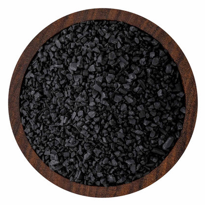 Top-down view of coarse black sea salt crystals in a round wooden bowl, showing jagged charcoal-black grains and textured wood rim.