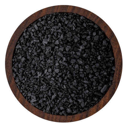 Top-down view of coarse black sea salt crystals in a round wooden bowl, showing jagged charcoal-black grains and textured wood rim.