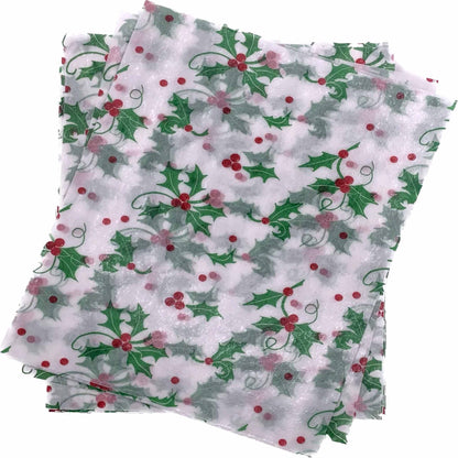 Overlapping stack of white 4" x 5" wax caramel wrappers printed with a repeating pattern of green holly leaves and red berries.