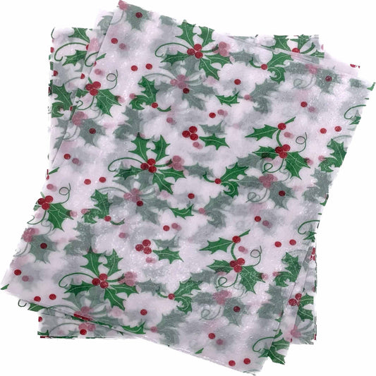 Overlapping stack of white 4" x 5" wax caramel wrappers printed with a repeating pattern of green holly leaves and red berries.
