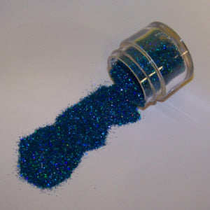 Blue Galaxy Glitter Dust poured from a clear jar, shimmering with ocean-inspired sparkle and hints of teal and sapphire