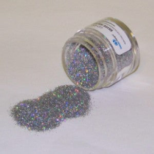 Holographic silver Galaxy Glitter Dust spilling from a jar, sparkling with multicolored rainbow reflections on a white surface.