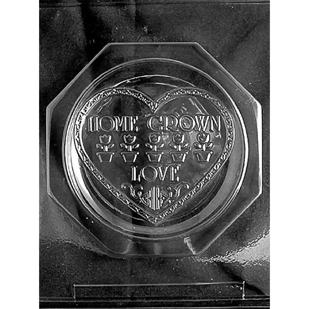 Clear two-piece chocolate mold featuring a round plate with a heart-shaped center, raised “Home Grown Love” lettering, potted flowers, and decorative borders.