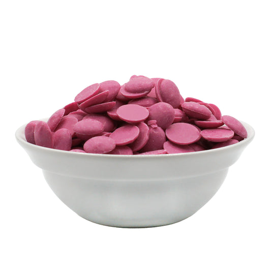 Pink candy melting wafers piled in a white bowl, side view on a white background.