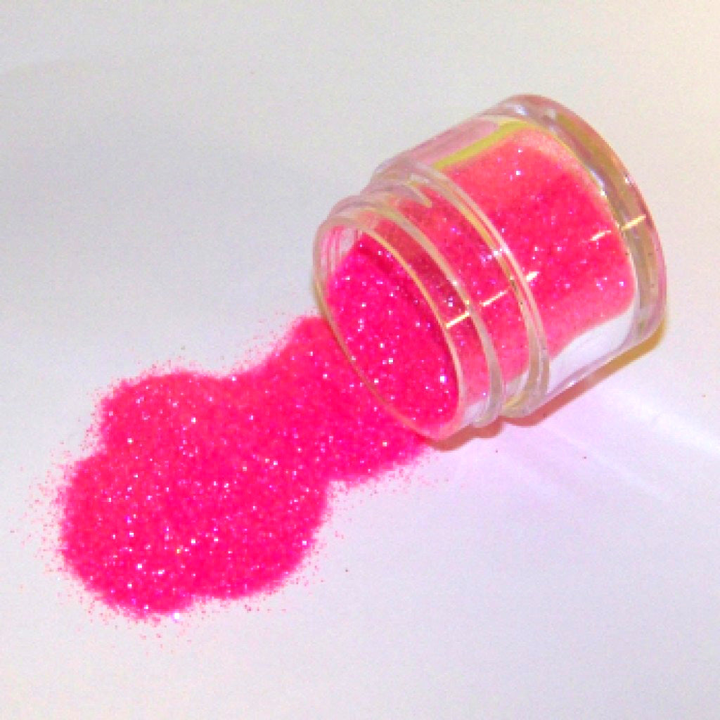 Small clear jar tipped on its side spilling bright hot pink glitter dust onto a white surface, with fine sparkling particles visible throughout.