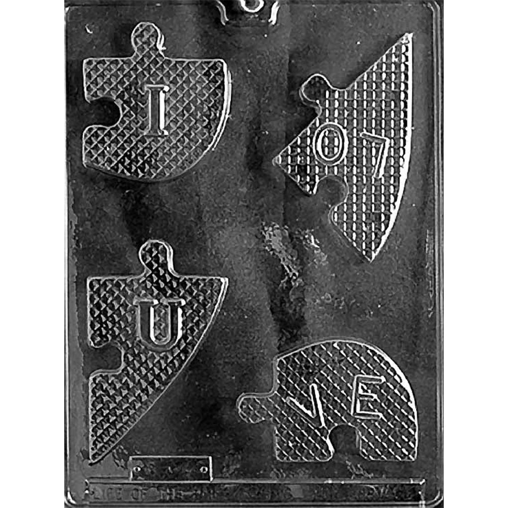 Clear plastic chocolate mold on a dark background with four heart puzzle-piece cavities featuring a diamond texture and raised letters that spell “I LOVE U” when assembled.