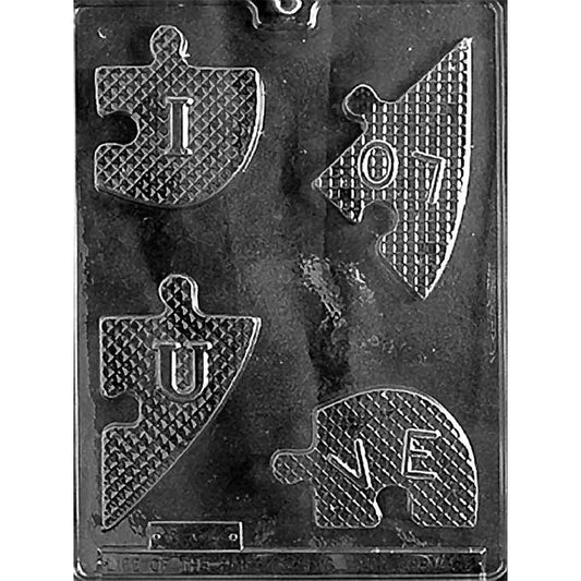 Clear plastic chocolate mold on a dark background with four heart puzzle-piece cavities featuring a diamond texture and raised letters that spell “I LOVE U” when assembled.