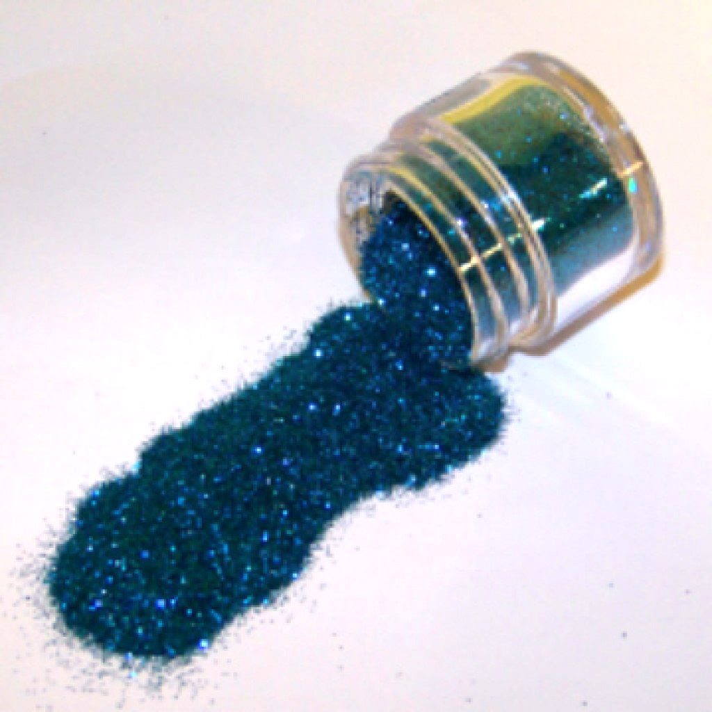Small clear jar tipped on its side spilling ice blue aquamarine glitter dust onto a white surface, with fine sparkling particles in a cool blue shade.