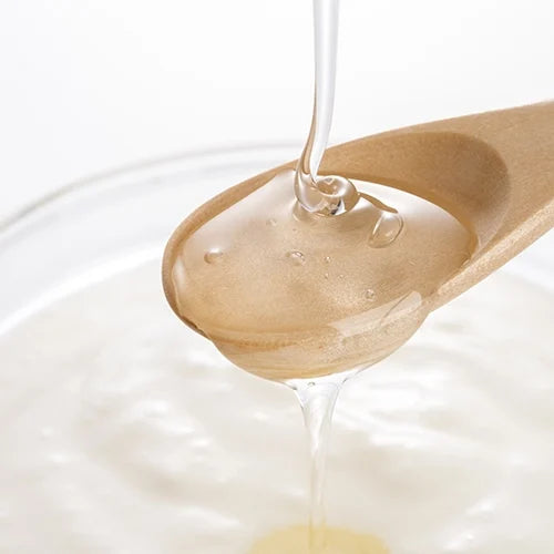 Close-up of clear liquid invert sugar being poured from a wooden spoon into a bowl, showing its smooth, syrupy texture.