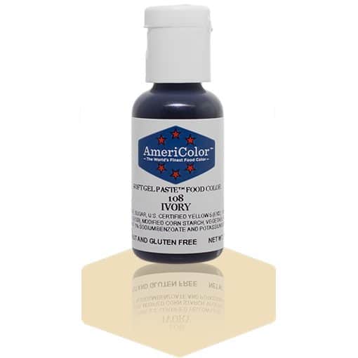 A bottle of AmeriColor Ivory soft gel paste food coloring with a white cap, blue label, and red stars, standing on a beige reflective surface with the bottle’s reflection visible.