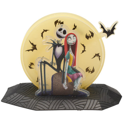 Jack and Sally cake topper sitting in front of a yellow moon with flying black bats, from The Nightmare Before Christmas.