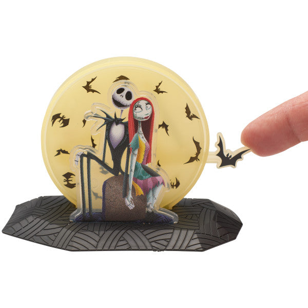 Hand adjusting the bat detail on The Nightmare Before Christmas cake topper featuring Jack, Sally, and a yellow moon with black bats.