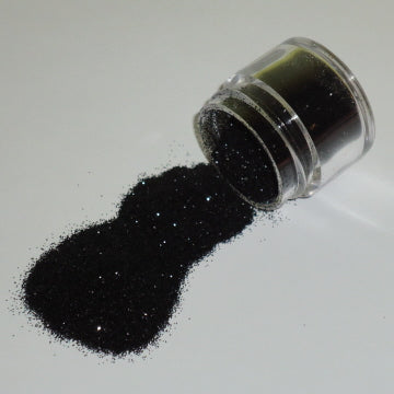 Small jar of black Galaxy Glitter Dust tipped over, spilling fine, sparkly black glitter onto a white surface.