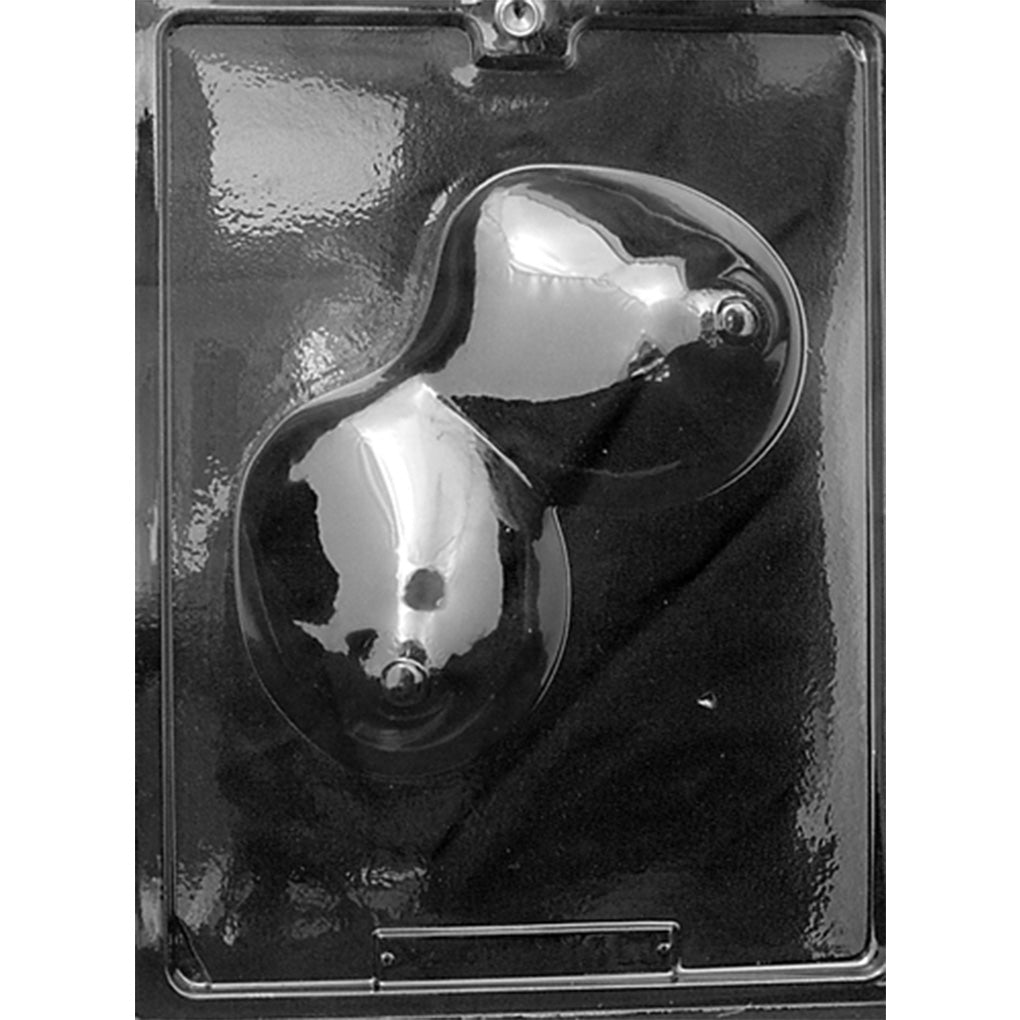 Clear plastic chocolate mold photographed against a black background with one large cavity shaped like a pair of breasts, featuring rounded contours and raised nipple details.