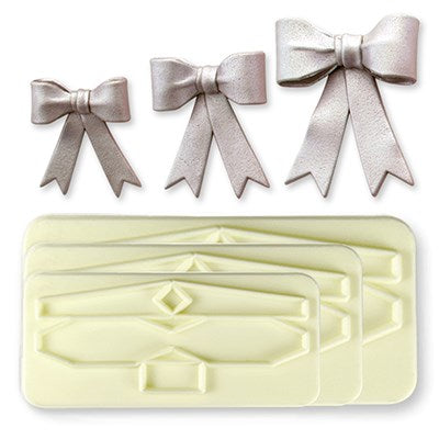 Three large fondant bows in silver next to a 3 piece large bow cutter set for cake decorating.