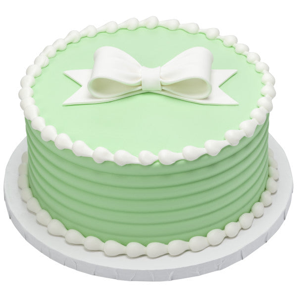 Round mint green cake with piped white frosting and a white gum paste bow centered on top.