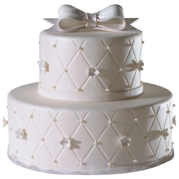 Elegant two-tier white cake with quilted fondant pattern and pearl accents, topped with a large white gum paste bow.