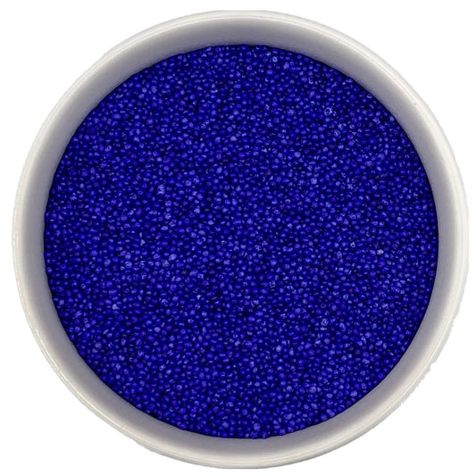 Top-down view of a white bowl filled with lavender non-pareils, showing tiny round sprinkle beads in a vivid blue-violet lavender shade.