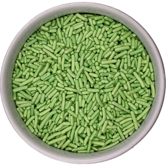 Top-down view of a round container filled with light green jimmies sprinkles, showing short rod-shaped pieces packed closely together.