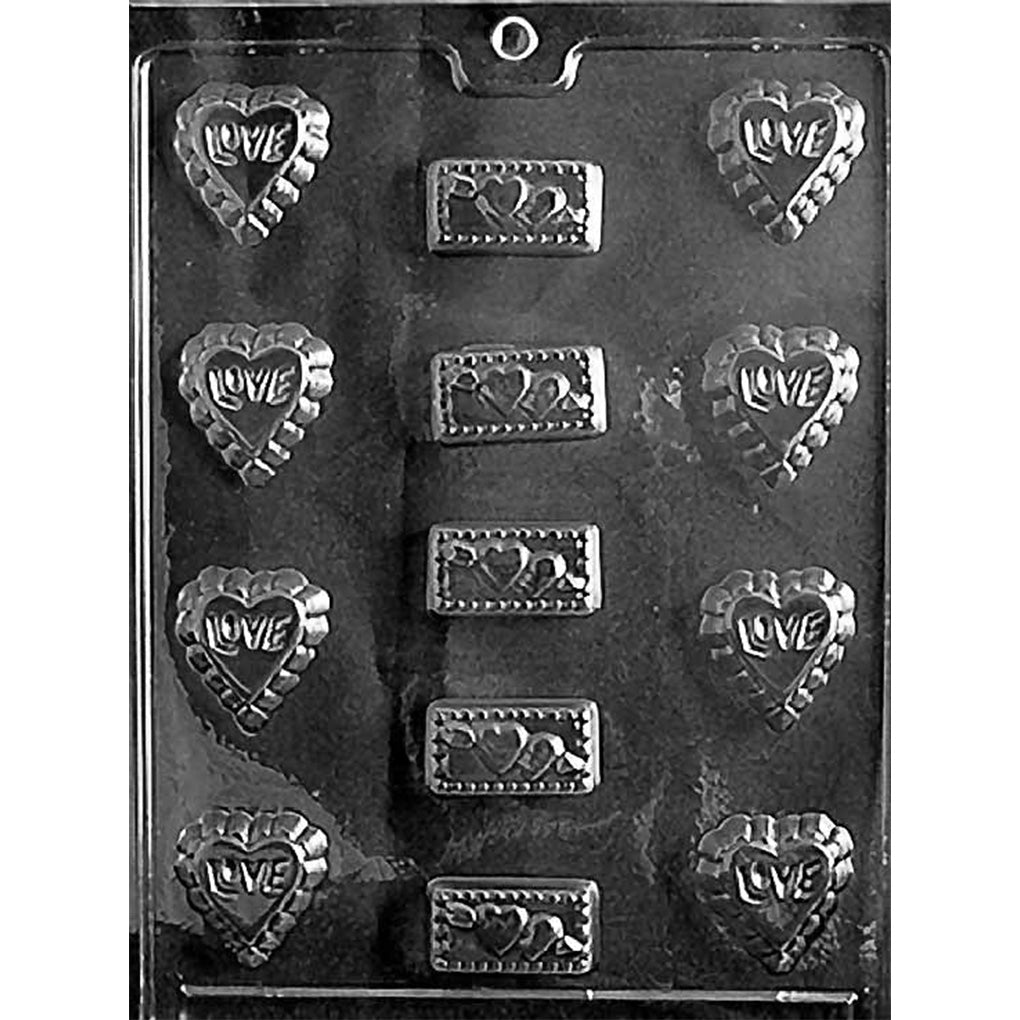 Clear plastic chocolate mold photographed on a black background with small heart cavities that read “LOVE” and rectangular bar cavities with raised heart details, arranged in rows.