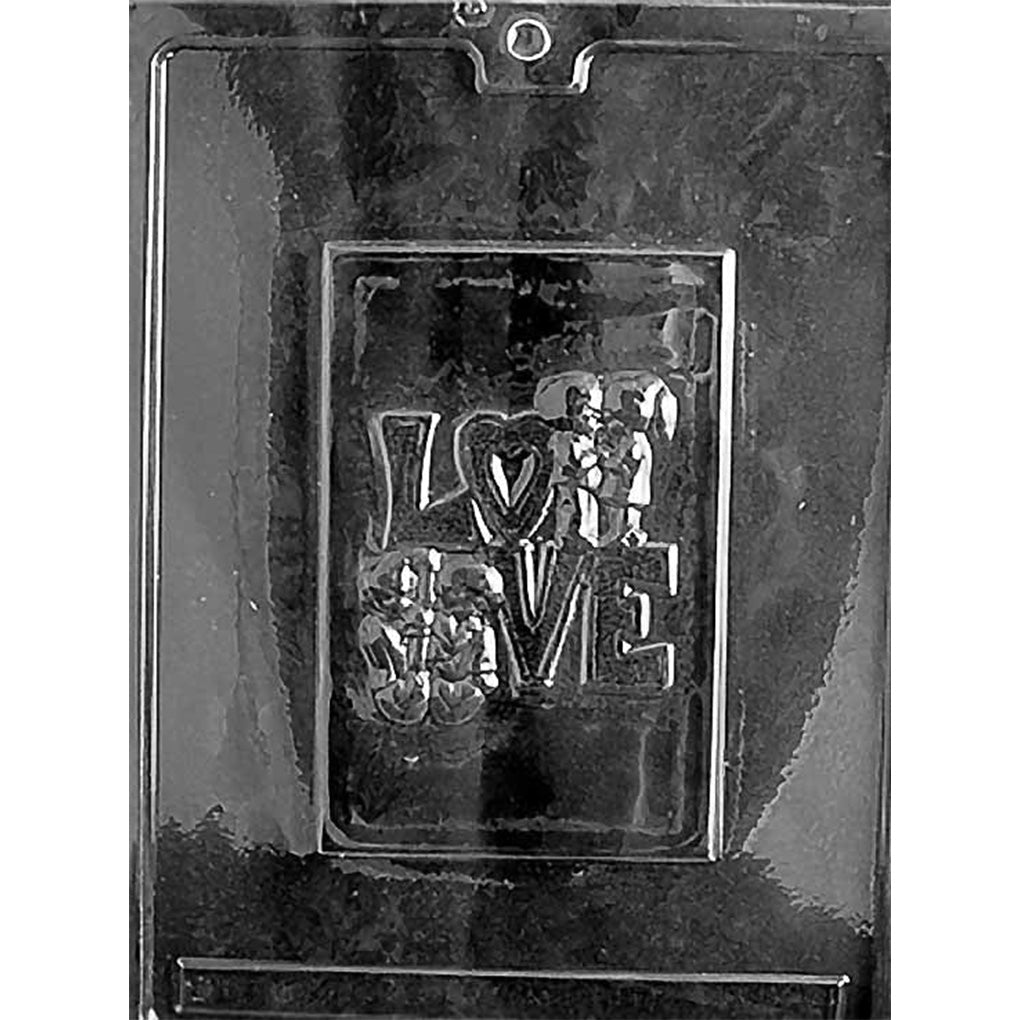 Clear plastic chocolate bar mold photographed on a dark background with one card-shaped cavity featuring raised LOVE letters and two small kid couple figures, one seated back-to-back and one holding hands.