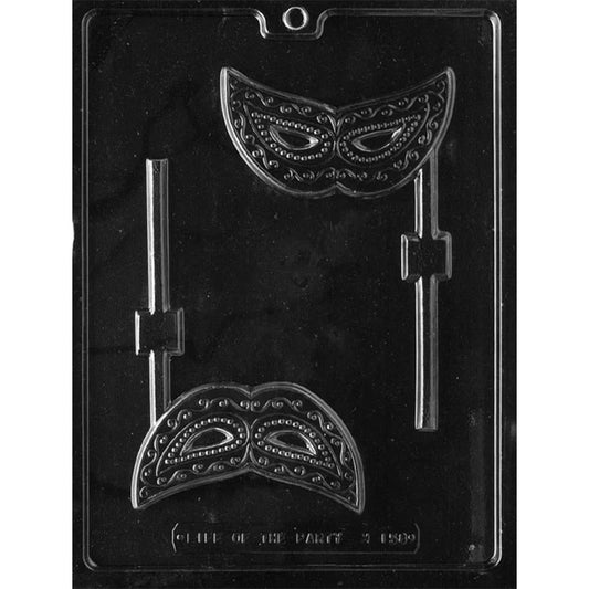 Clear plastic chocolate lollipop mold with two masquerade mask cavities featuring raised swirls, beaded details, eye openings, and lollipop stick channels on a dark background.