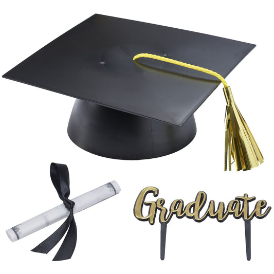 Graduation cake topper set with a black mortarboard cap, yellow rope and metallic gold tassel, a rolled white diploma tied with a black ribbon, and a black-and-gold “Graduate” script pick.