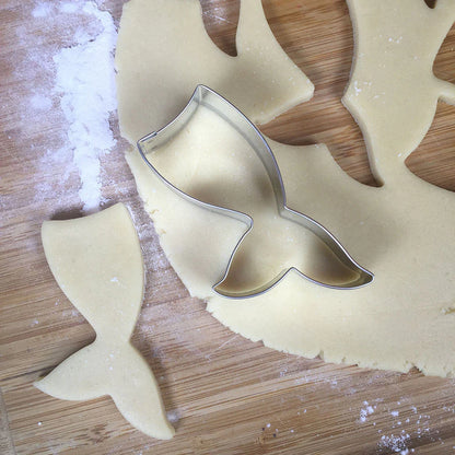 A close-up of the Mermaid Tail Cookie Cutter being used to cut out dough on a floured surface, showcasing its precise shape and design.