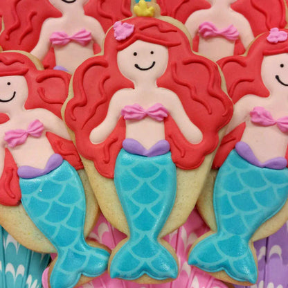 Decorated mermaid cookies with red hair, a pink seashell top, and a shimmering blue tail.