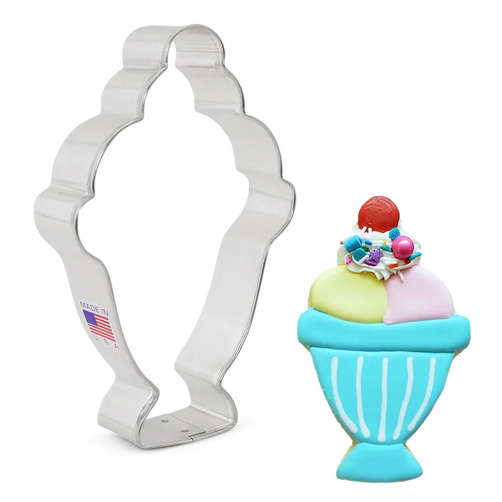 Cookie cutter next to a decorated sundae-shaped cookie with scoops of ice cream, sprinkles, and a cherry on top.