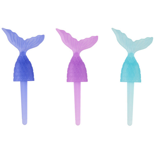 Close-up of three mermaid tail cupcake picks in translucent teal, pink, and purple with scale details and pointed sticks.