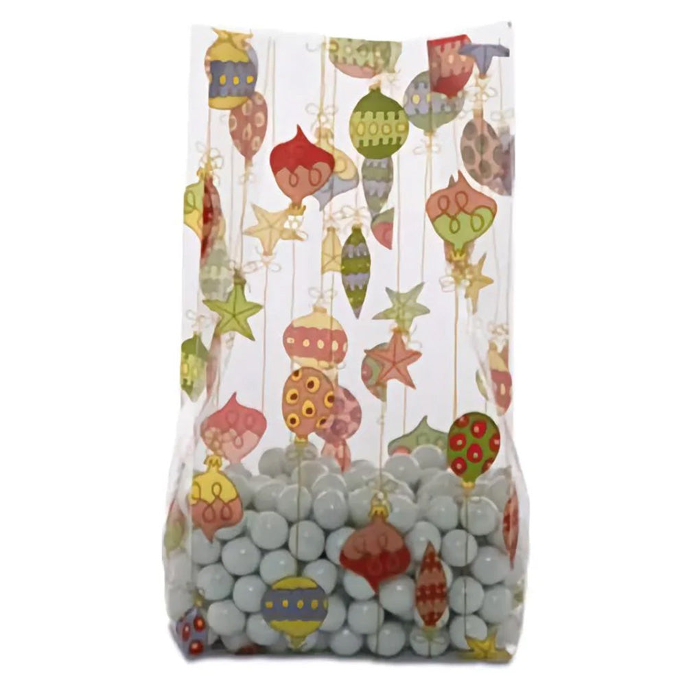 Clear cello treat bag with a colorful Christmas ornament and star print, shown filled with light gray candy balls and standing upright.