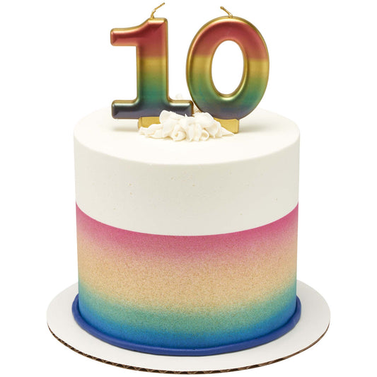 Two metallic rainbow number candles forming “10” on top of a tall ombré cake, with white frosting on top and a blue border at the base.