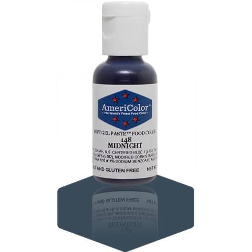 A bottle of AmeriColor Midnight soft gel paste food coloring with a white cap, blue label, and red stars, positioned on a dark blue reflective surface with the bottle’s reflection visible.