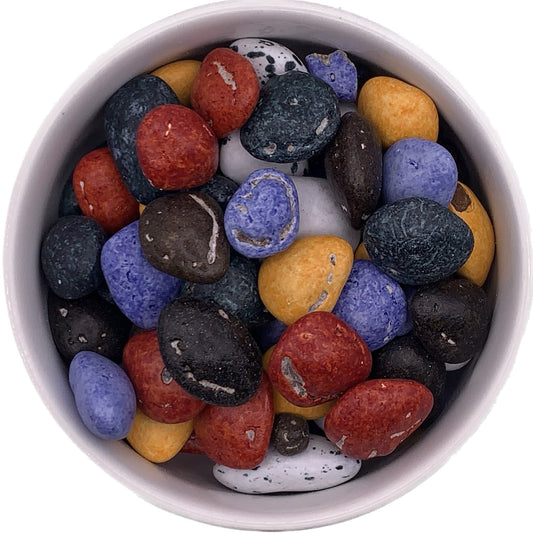 Colorful candy-coated milk chocolate river rocks in a white container, featuring realistic textures and colors resembling natural stones in red, yellow, purple, black, and white