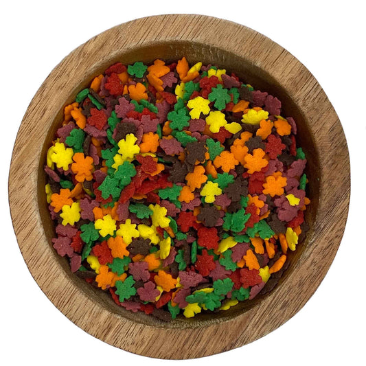 Close-up of mini autumn leaf quins sprinkles in red, orange, yellow, and brown, packaged in a 4 oz container.