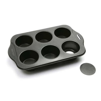 Empty six-cavity mini cheesecake pan photographed on a white background with one round removable bottom disk placed beside the pan.